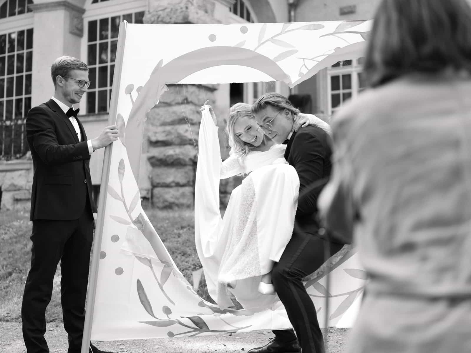 Guest holding heart frame while couple poses behind at Schloss Kartzow wedding, black and white
