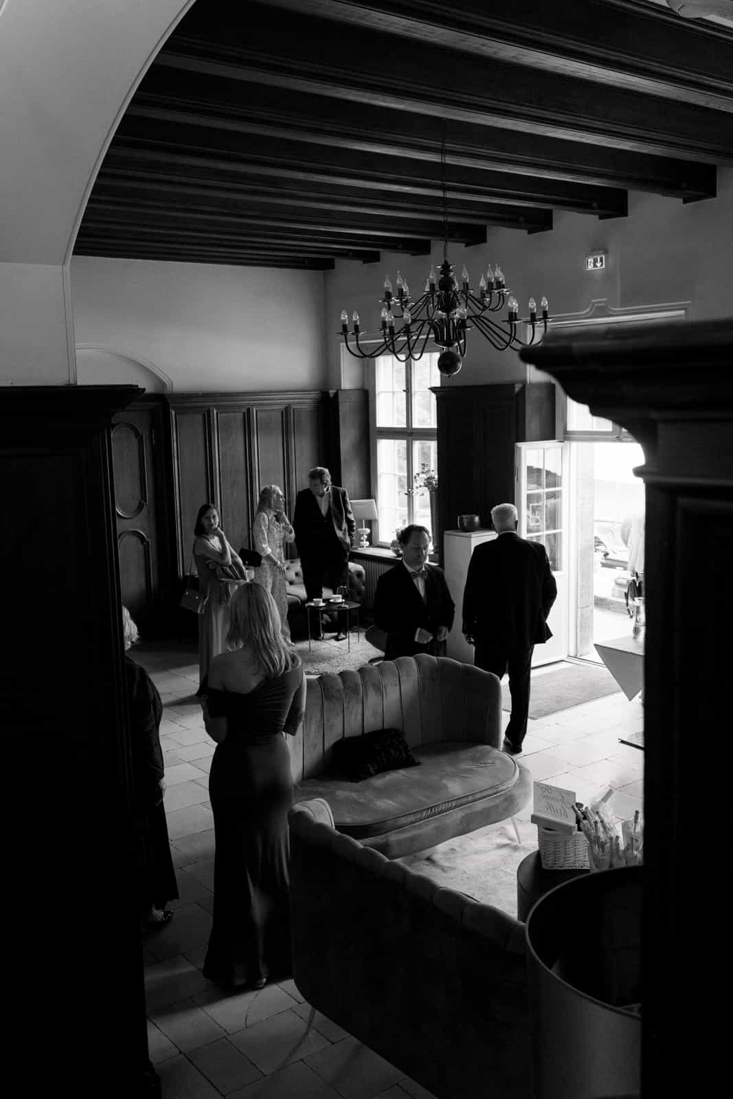 Wedding guests in historic manor house with wood paneling and chandelier, black and white