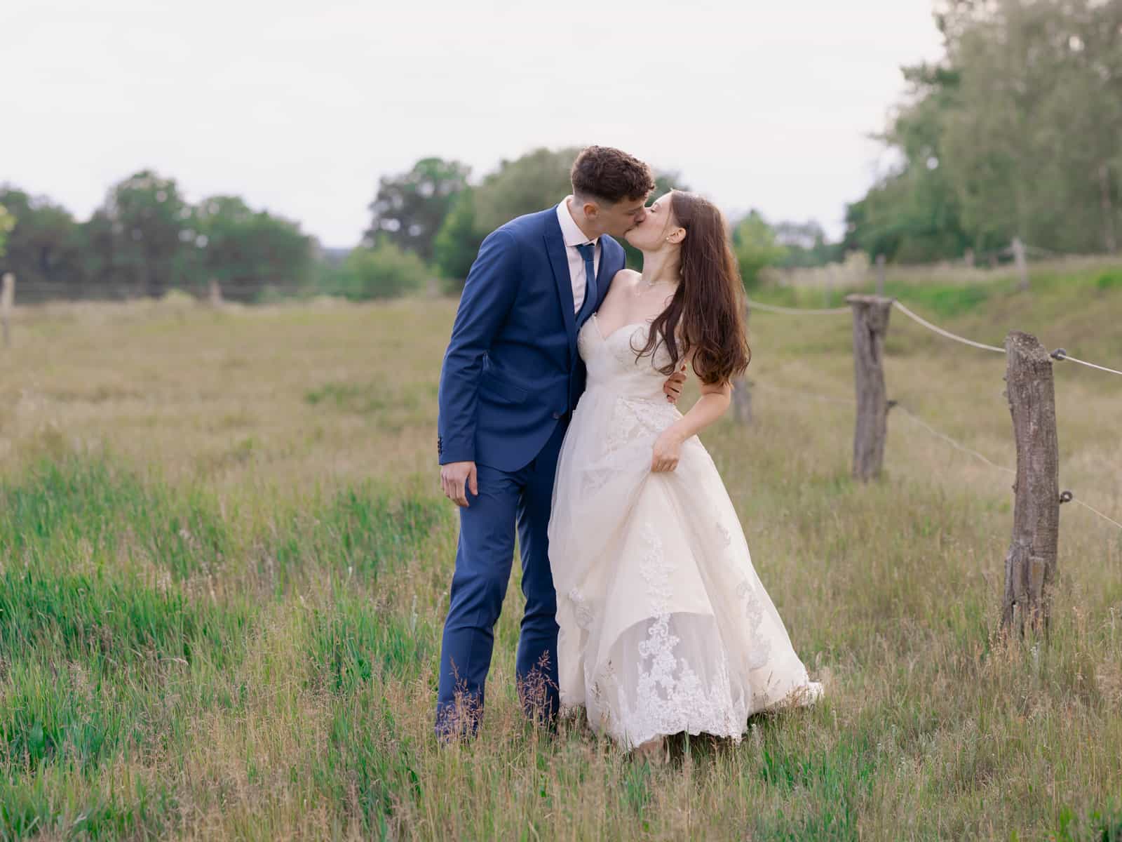 Couple kissing tenderly on sunny meadow by pasture fence