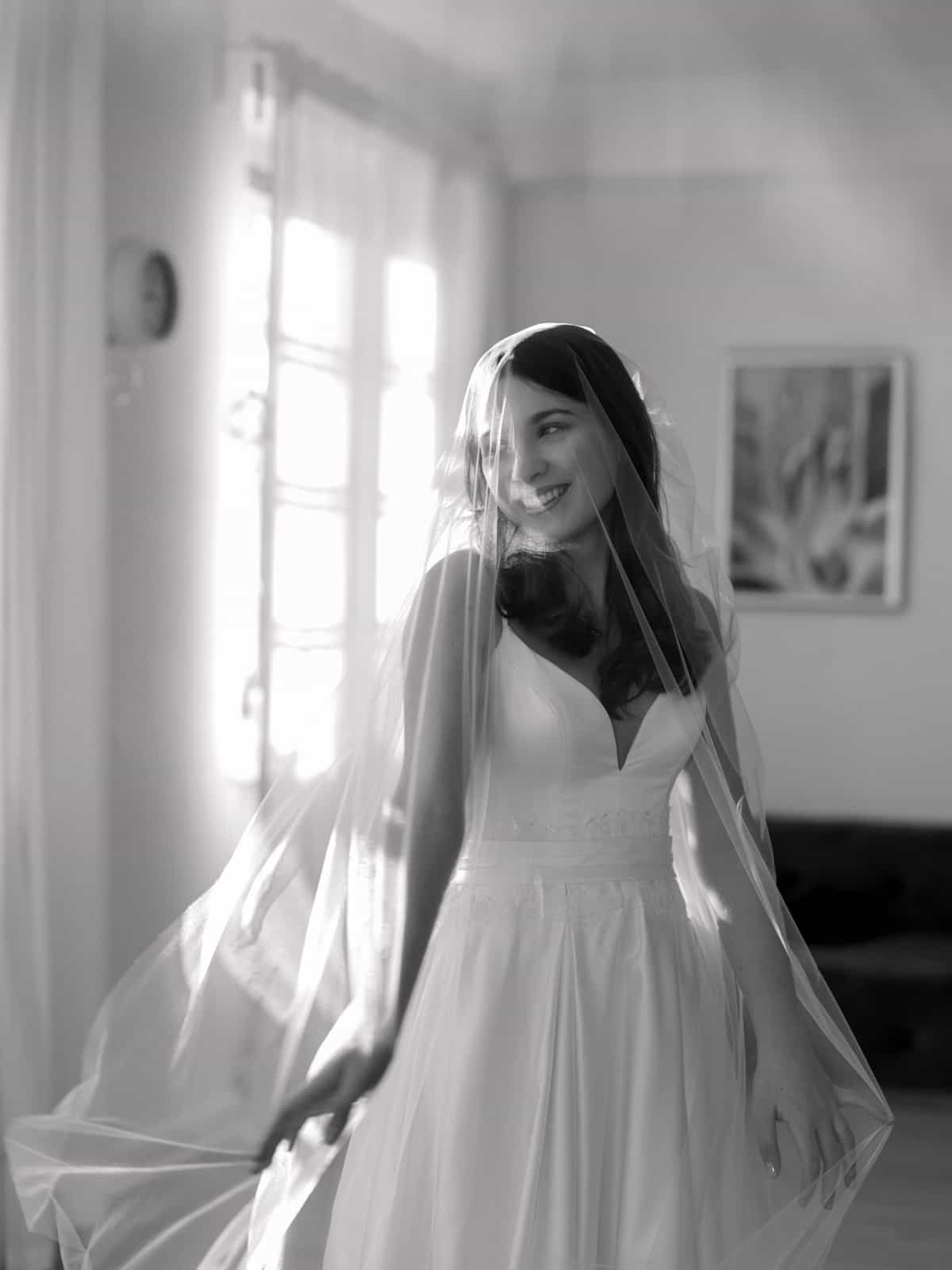Smiling bride with veil in window light in classic black and white