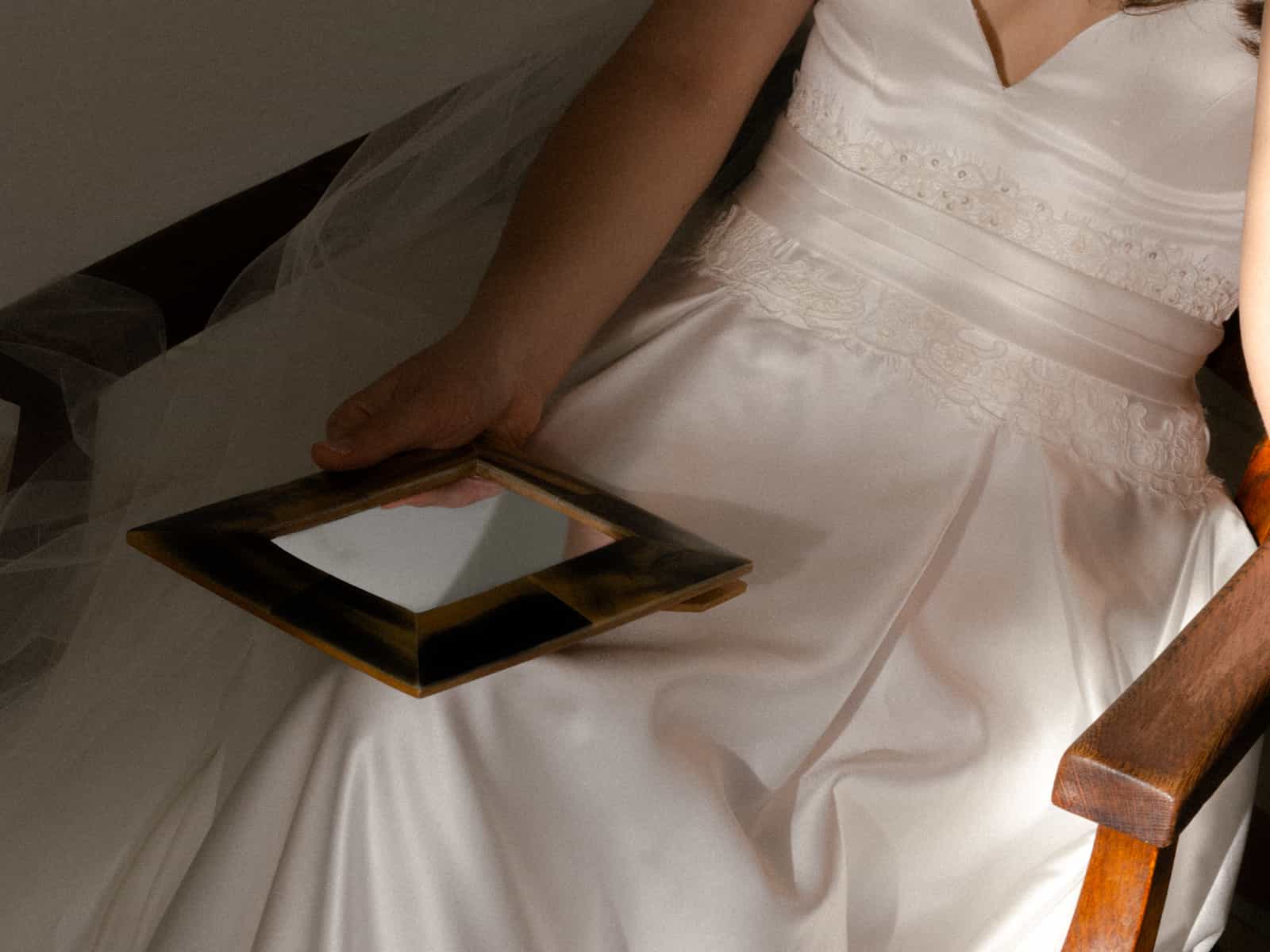 Bride in satin dress with lace details holding antique mirror