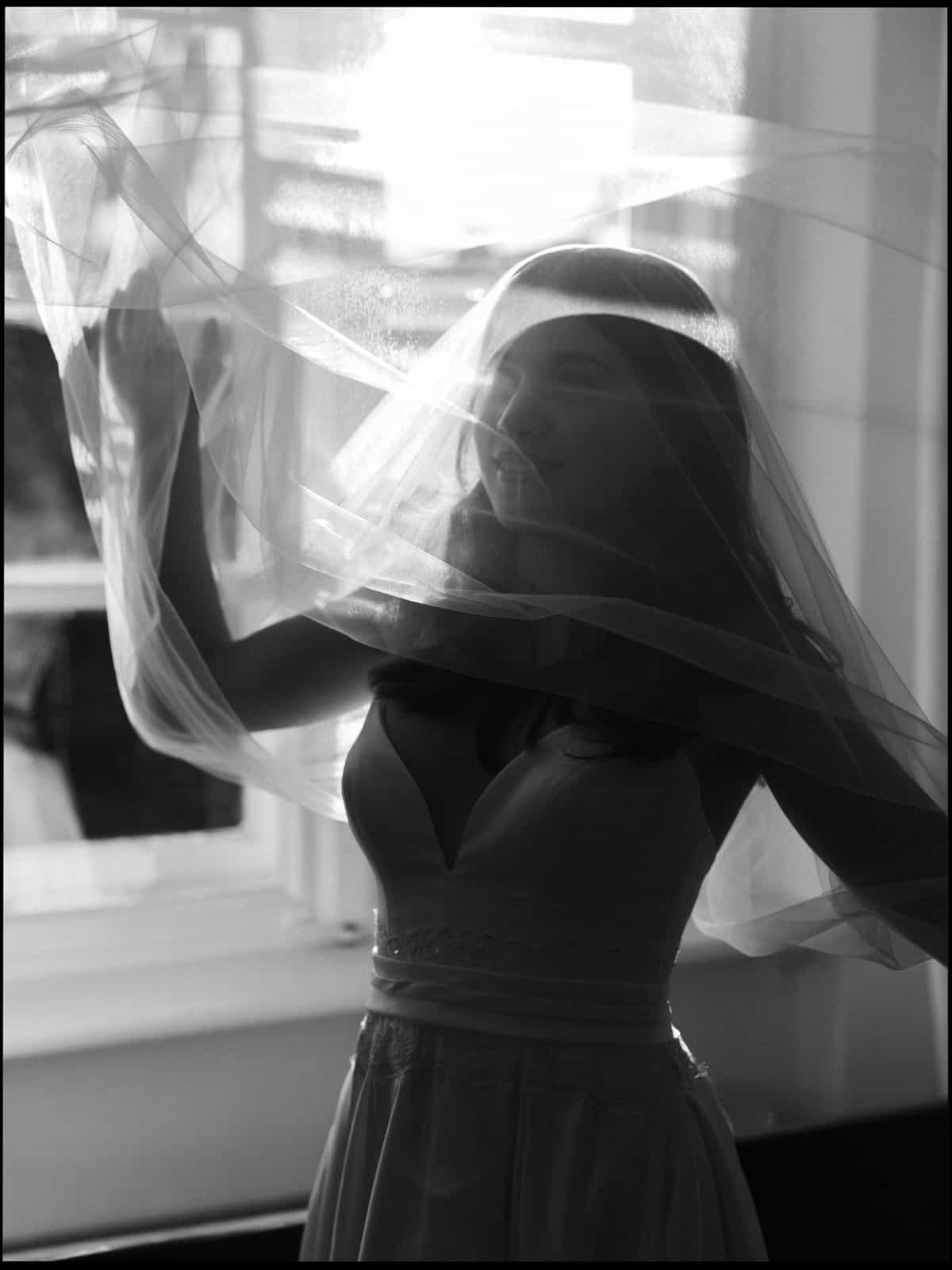 Bride with flowing veil by window in dramatic black and white