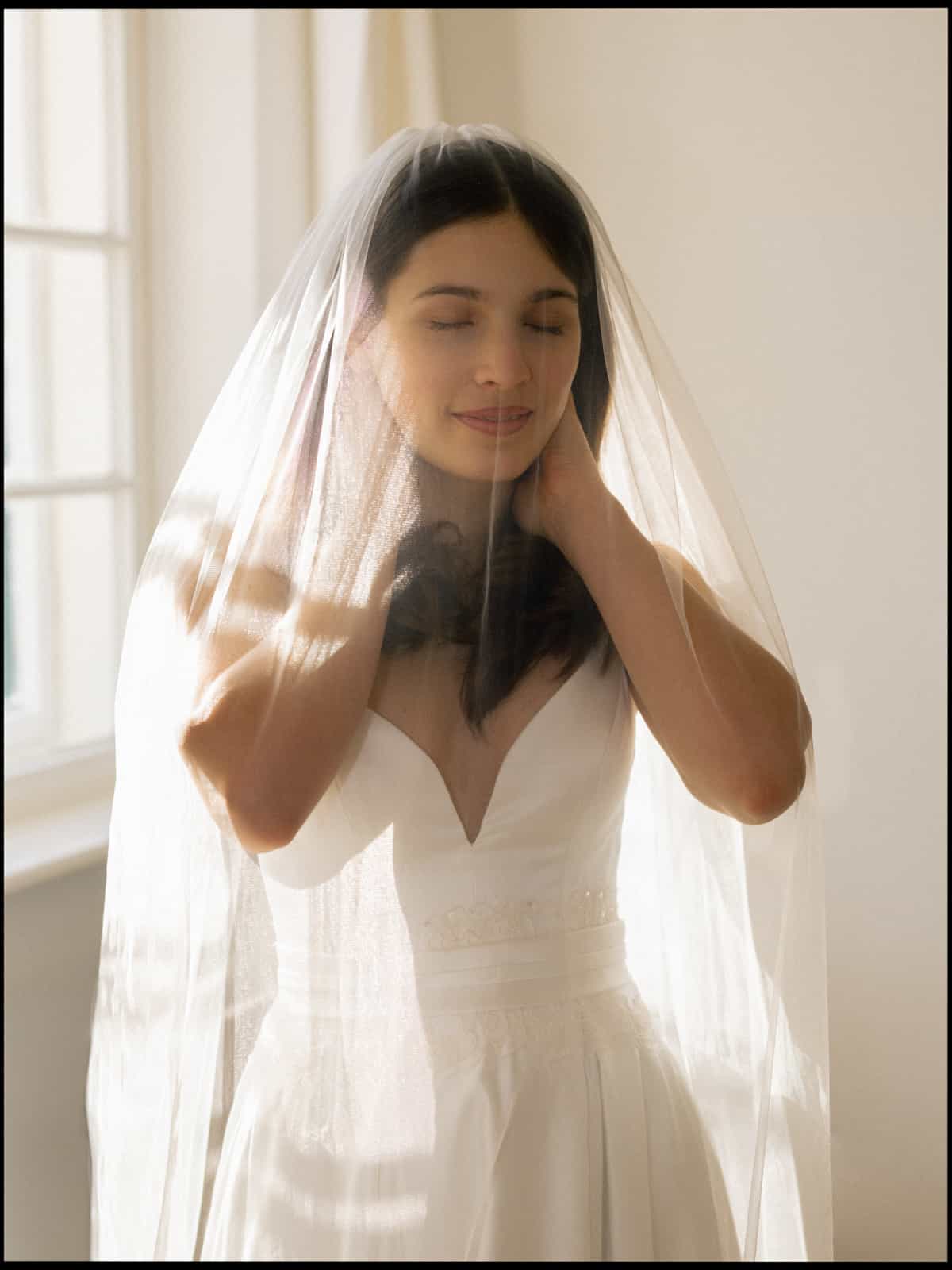 Dreamy bride with closed eyes under veil in soft light