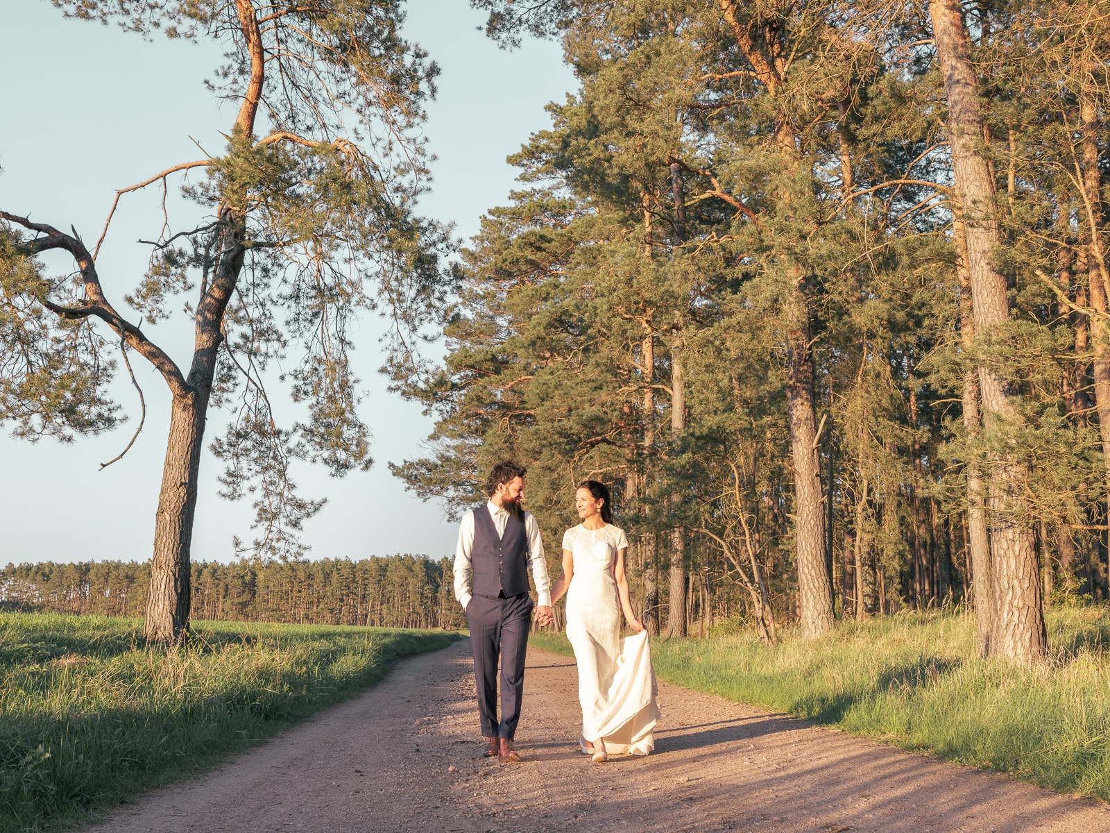 Brautpaar geht Hand in Hand über Feldweg bei goldenem Sonnenuntergang