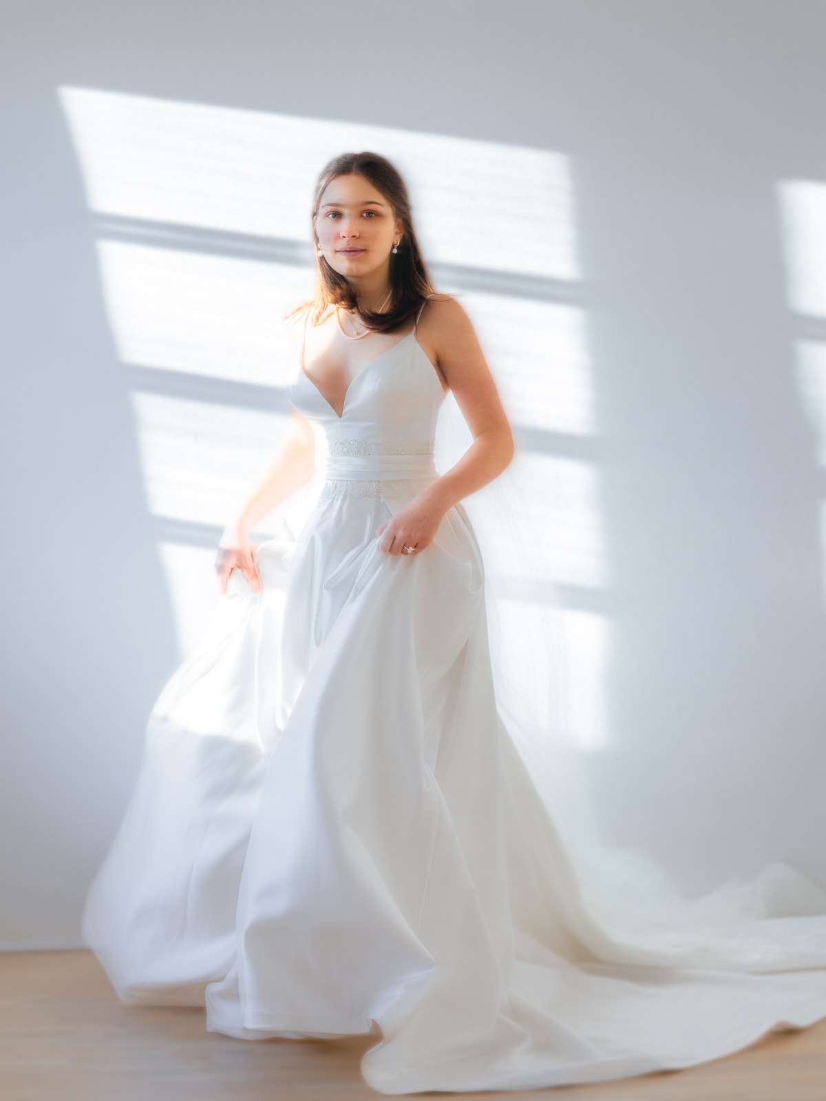 Junge Braut in elegantem weißen Kleid mit natürlichem Fensterlicht