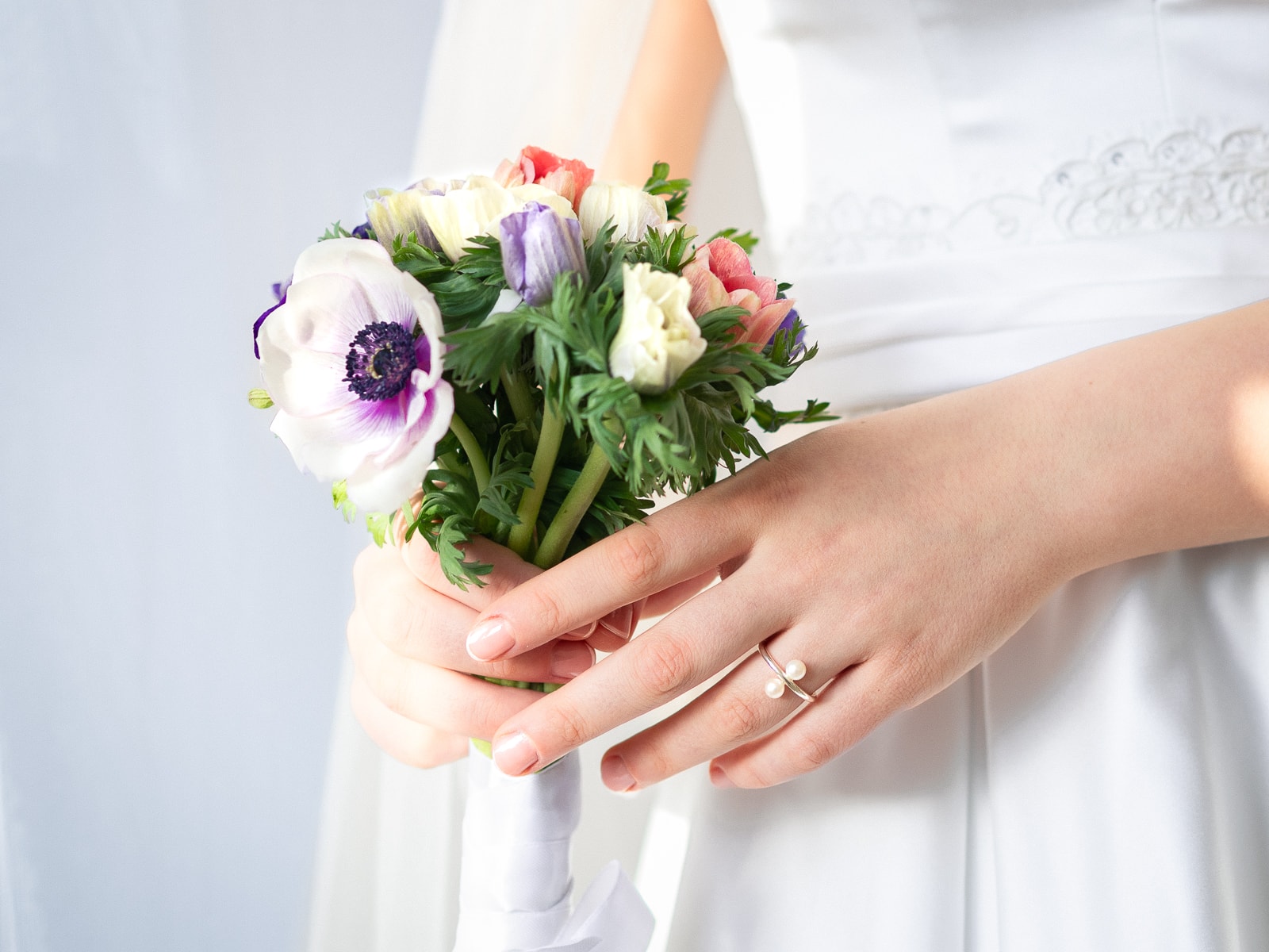 Bridal hands with anemone bouquet in purple, white and pink tones