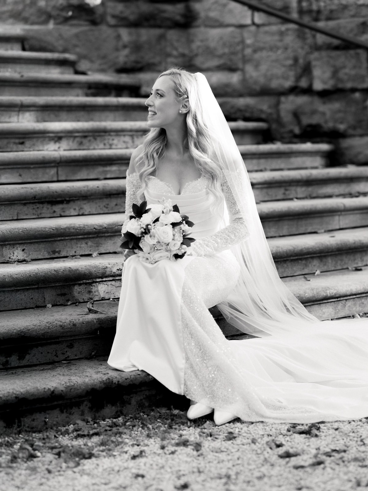 Bride in elegant lace dress with veil and bouquet on stone stairs - Schloss Kartzow wedding photography