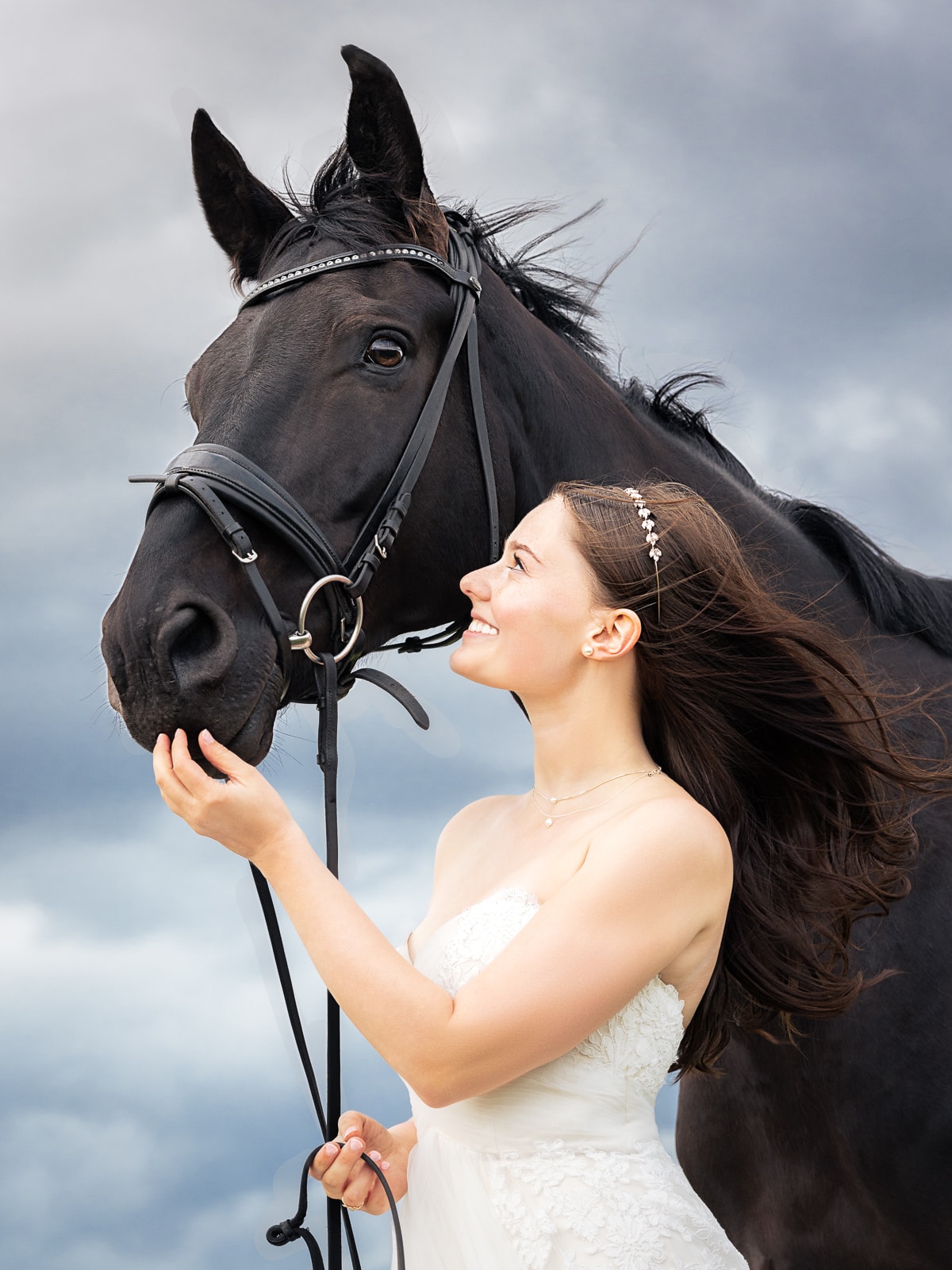 Bride with pearl headband smiling next to black horse with rhinestone bridle