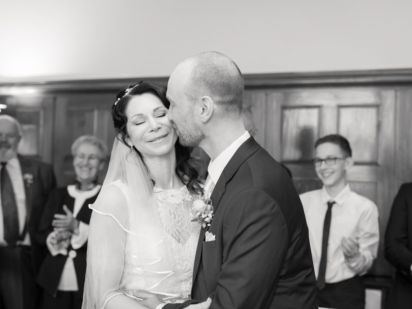 Groom kissing bride on cheek after ceremony with applauding guests