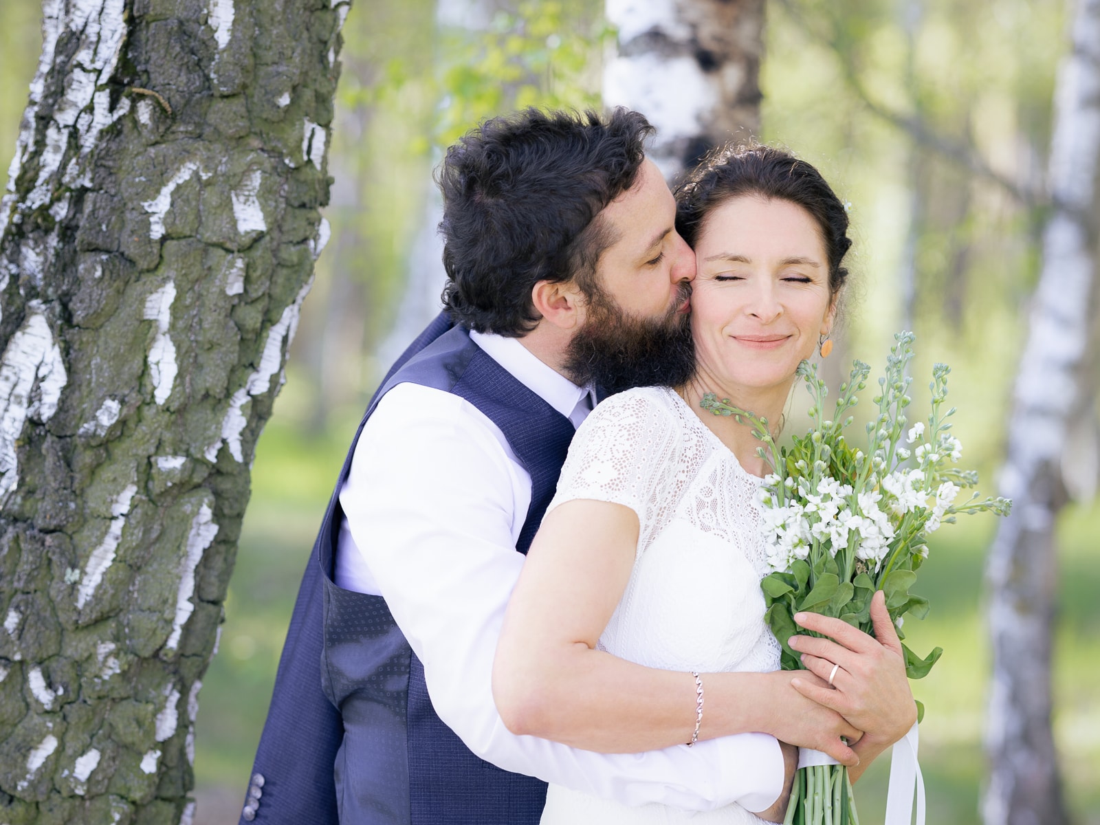 Groom kissing bride's forehead while she holds flower bouquet