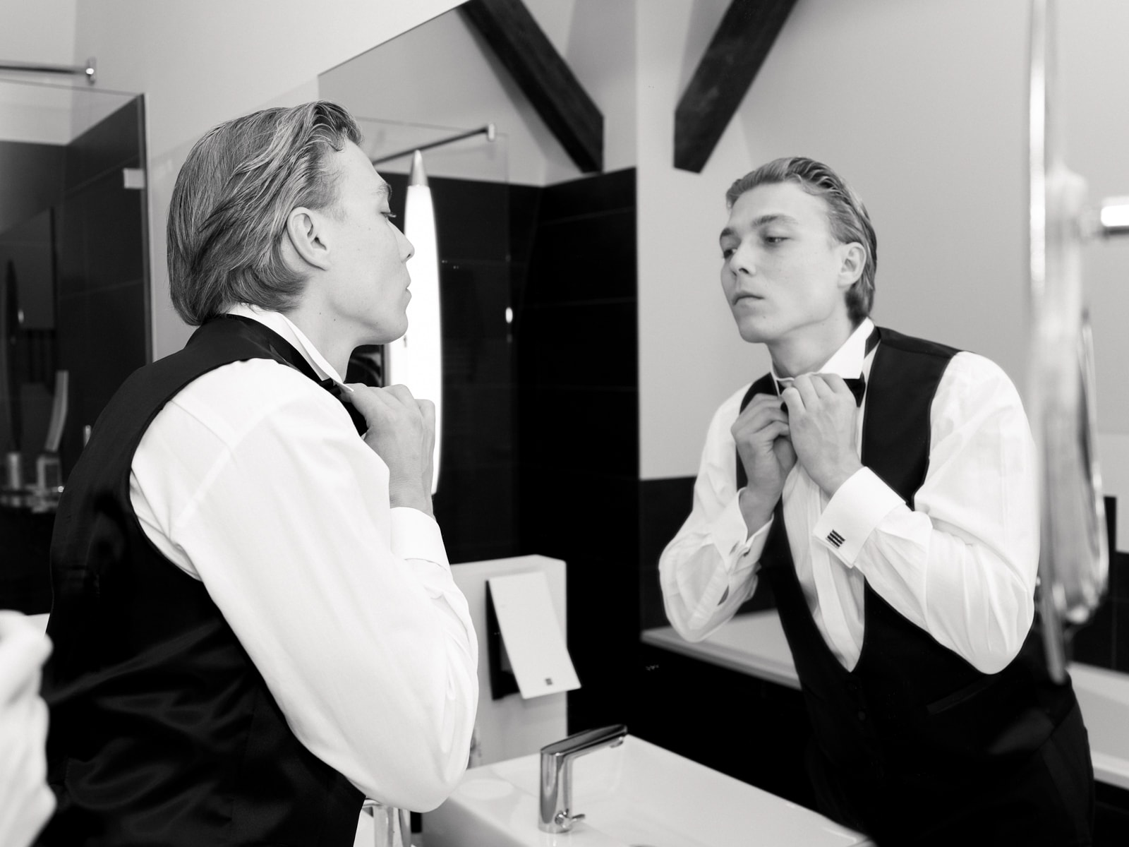 Groom in tuxedo tying bow tie in front of mirror, getting ready wedding photography Schloss Kartzow