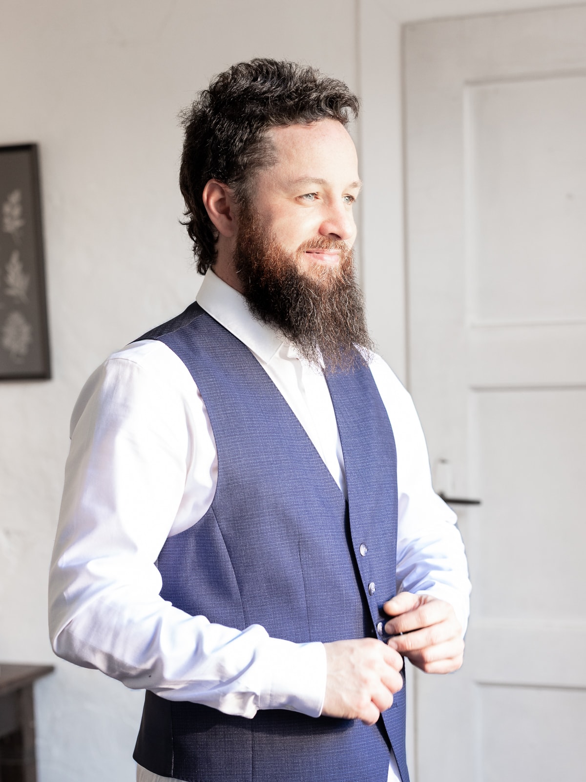 Bearded groom in blue vest by bright window