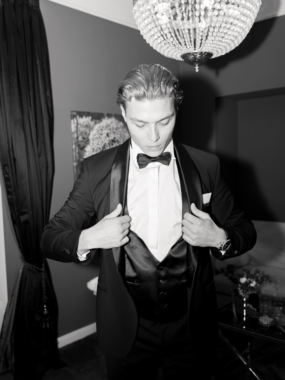 Groom putting on tuxedo jacket under chandelier, getting ready photography Schloss Kartzow