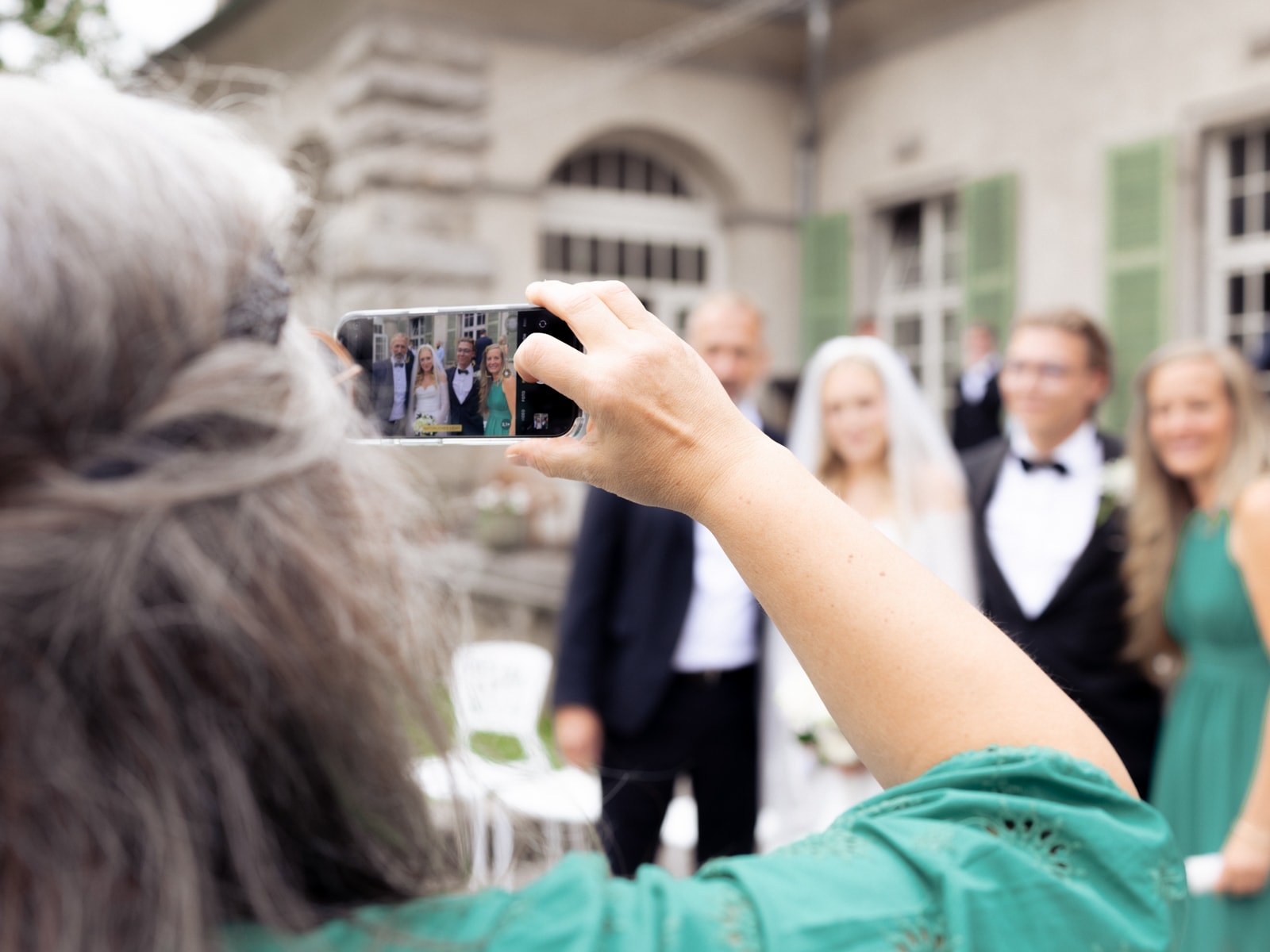 Guest photographing bride, groom and wedding party with smartphone at Schloss Kartzow castle wedding