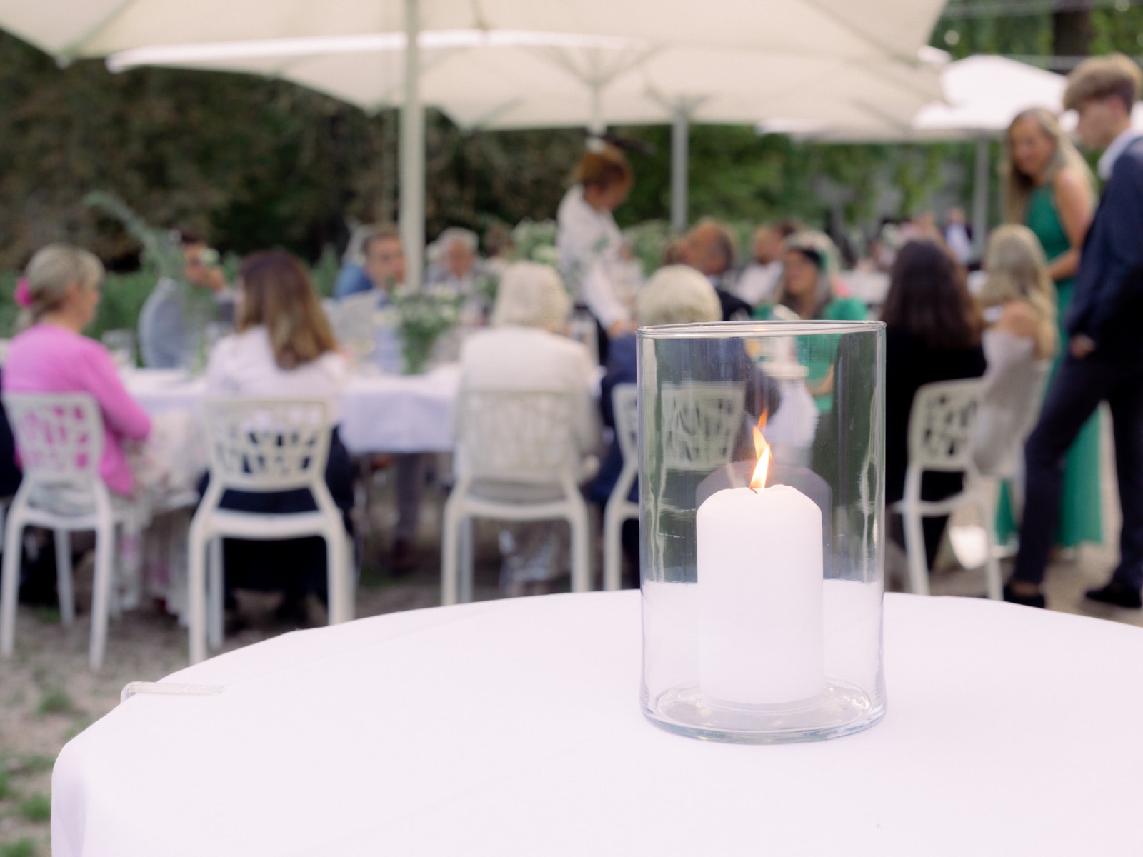 Candle in glass with blurred wedding guests in garden - outdoor wedding at Schloss Kartzow
