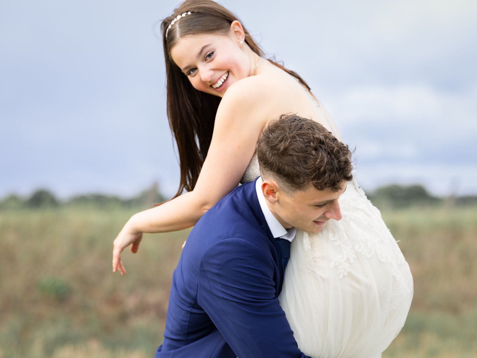 Laughing bride on groom's back on field path
