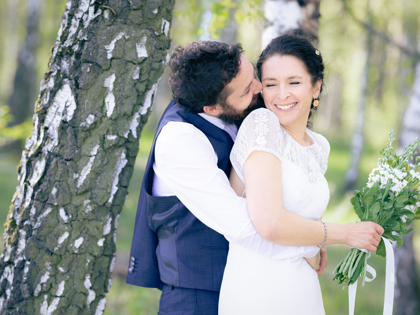 Radiant bride with flower bouquet receiving kiss from groom
