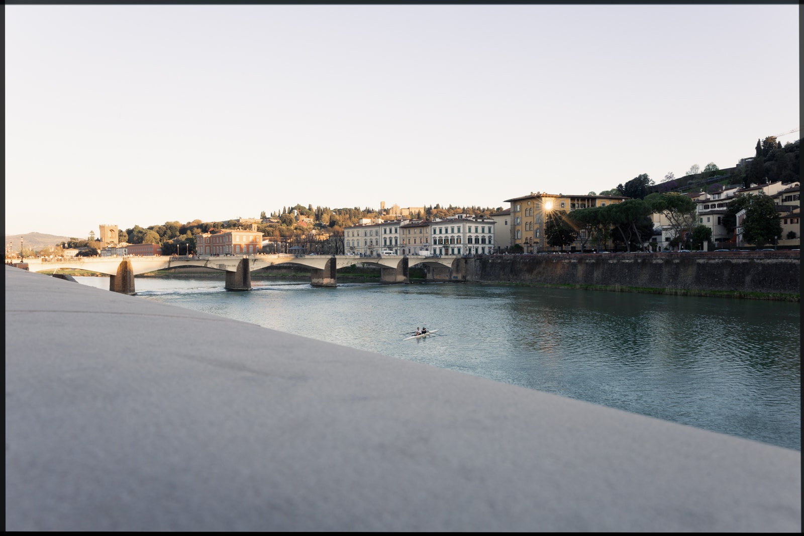 Florence riverside at golden hour with rowers on the Arno