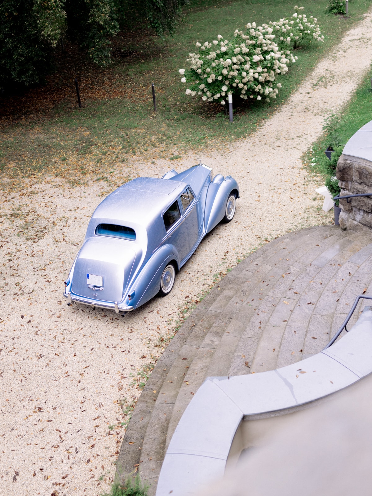 Blue vintage car on castle courtyard with white roses in background, wedding photography Schloss Kartzow