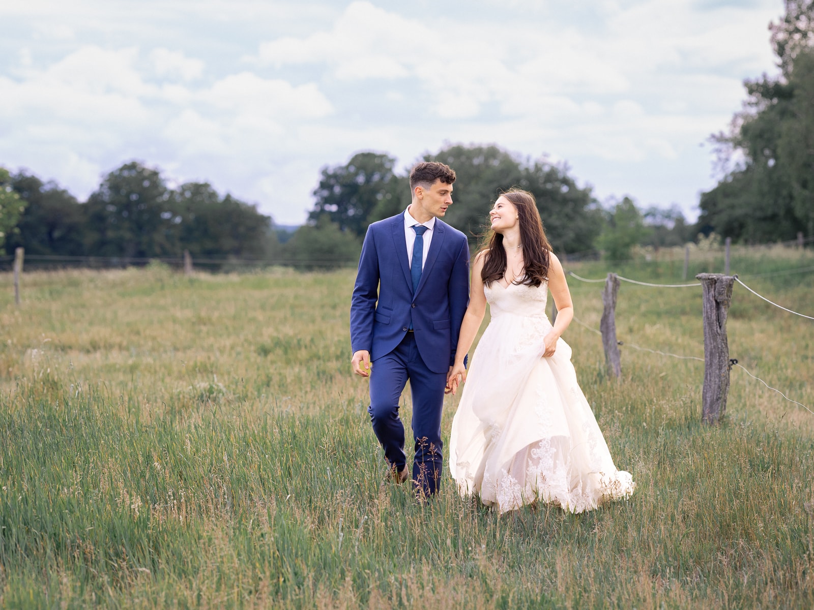 Couple walking hand in hand on field path with pasture fence