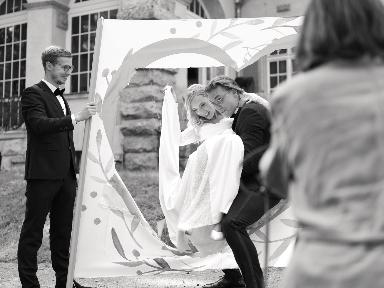Guest holding heart frame while couple poses behind at Schloss Kartzow wedding, black and white