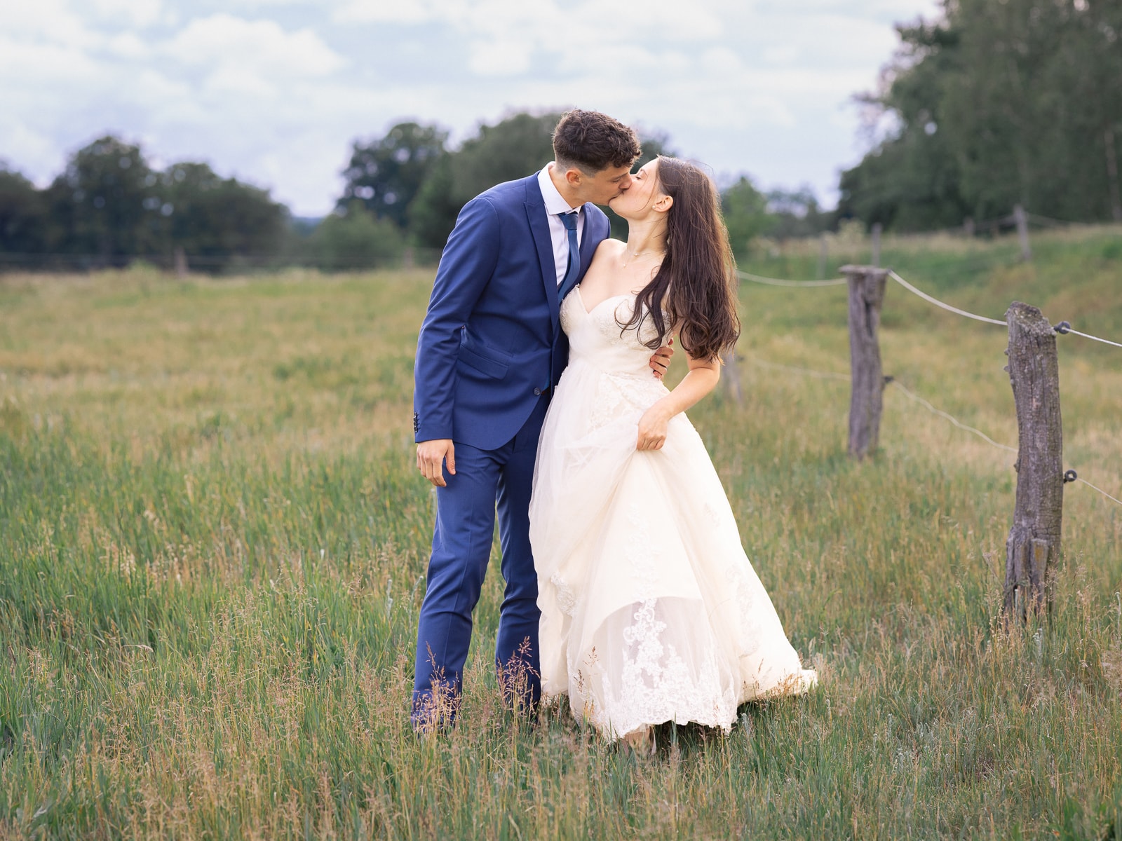 Couple kissing tenderly on sunny meadow by pasture fence