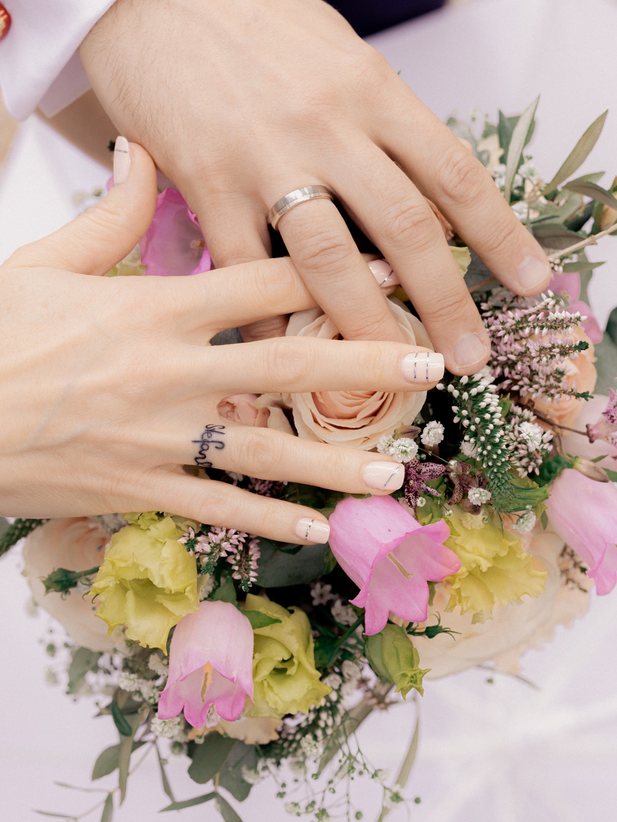 Hands with wedding rings on pink and white bridal bouquet