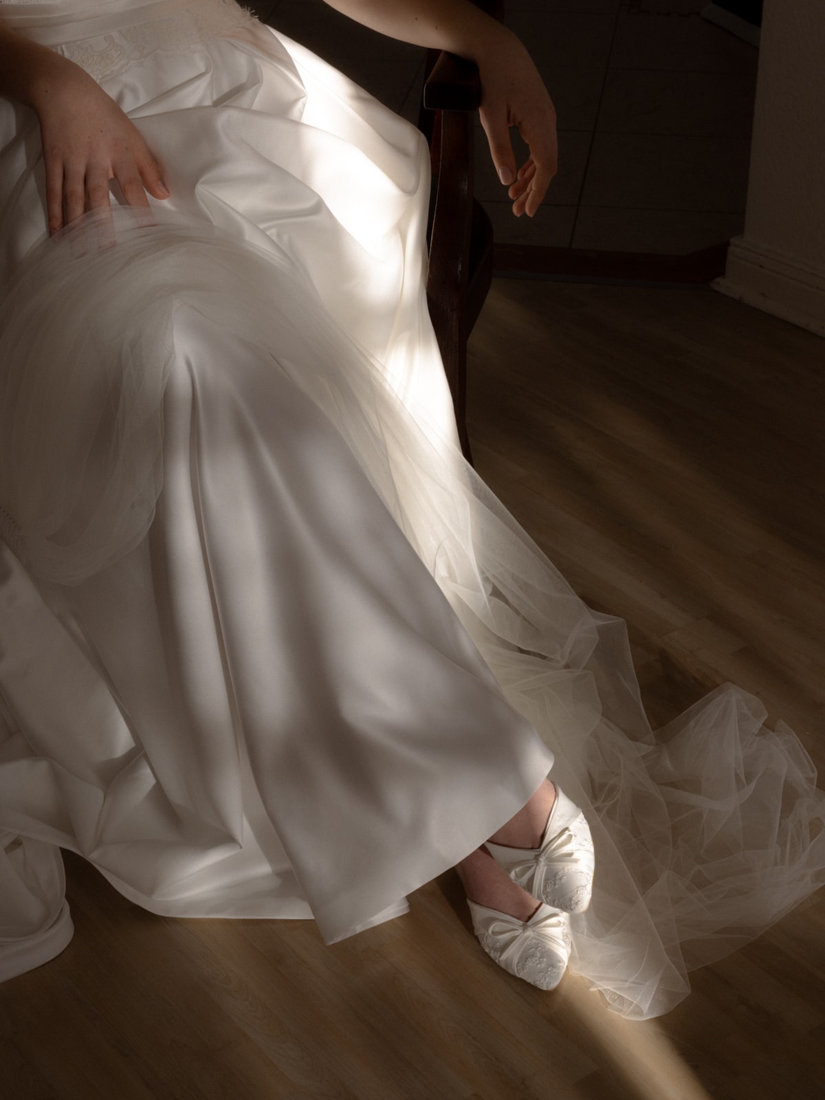 Detail shot of satin wedding dress with white bow bridal shoes on wooden floor