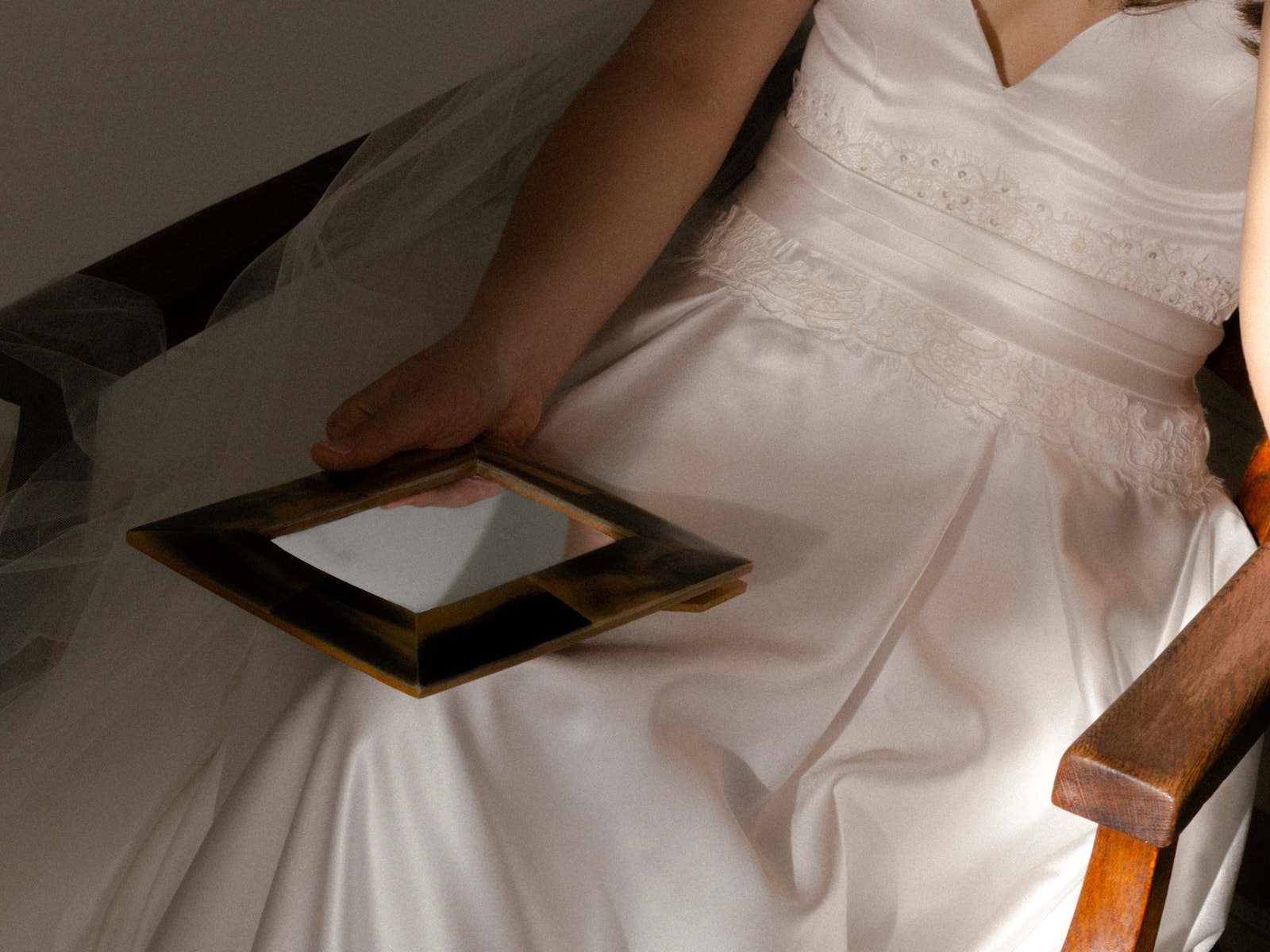 Bride in satin dress with lace details holding antique mirror