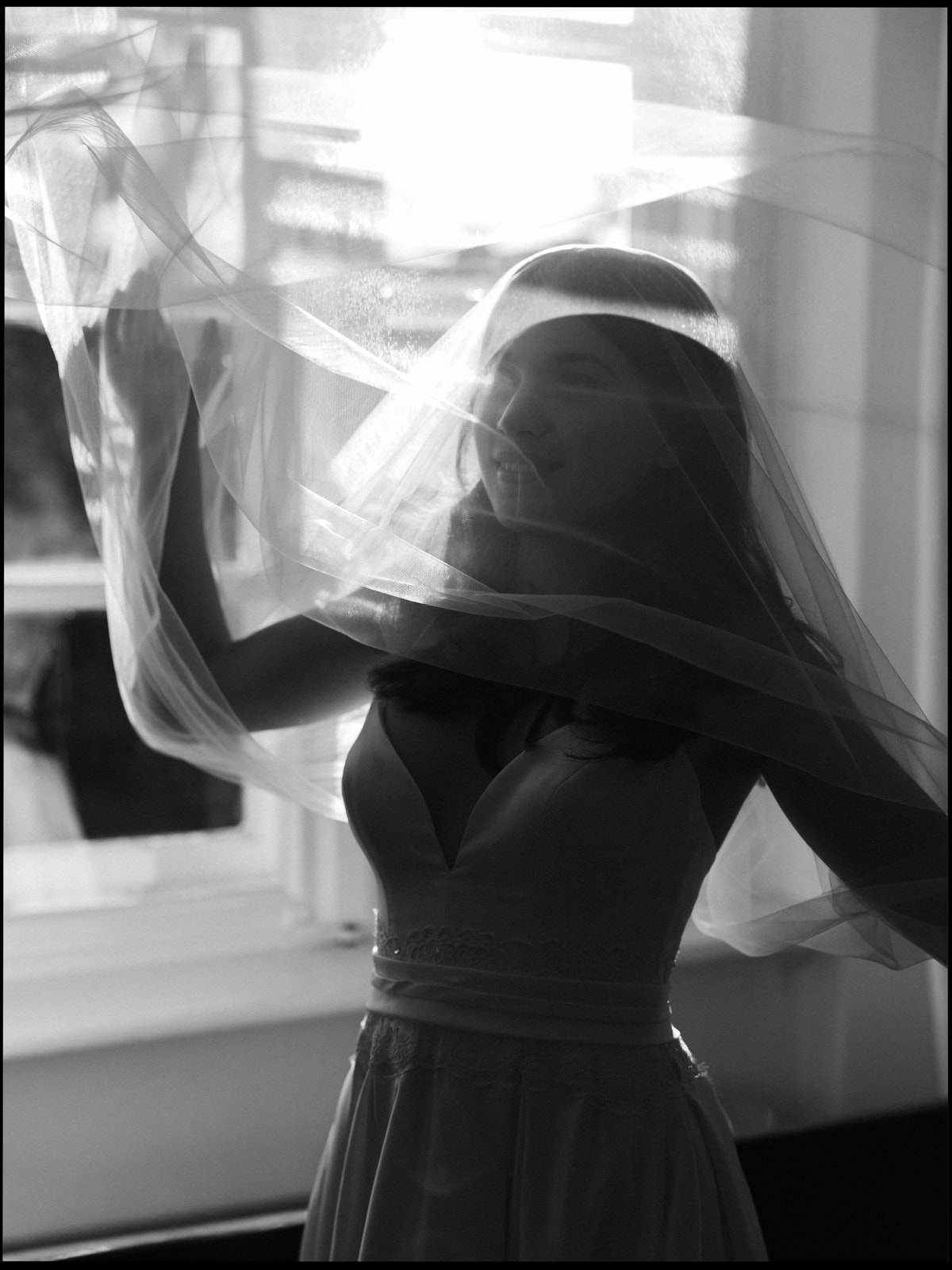 Bride with flowing veil by window in dramatic black and white