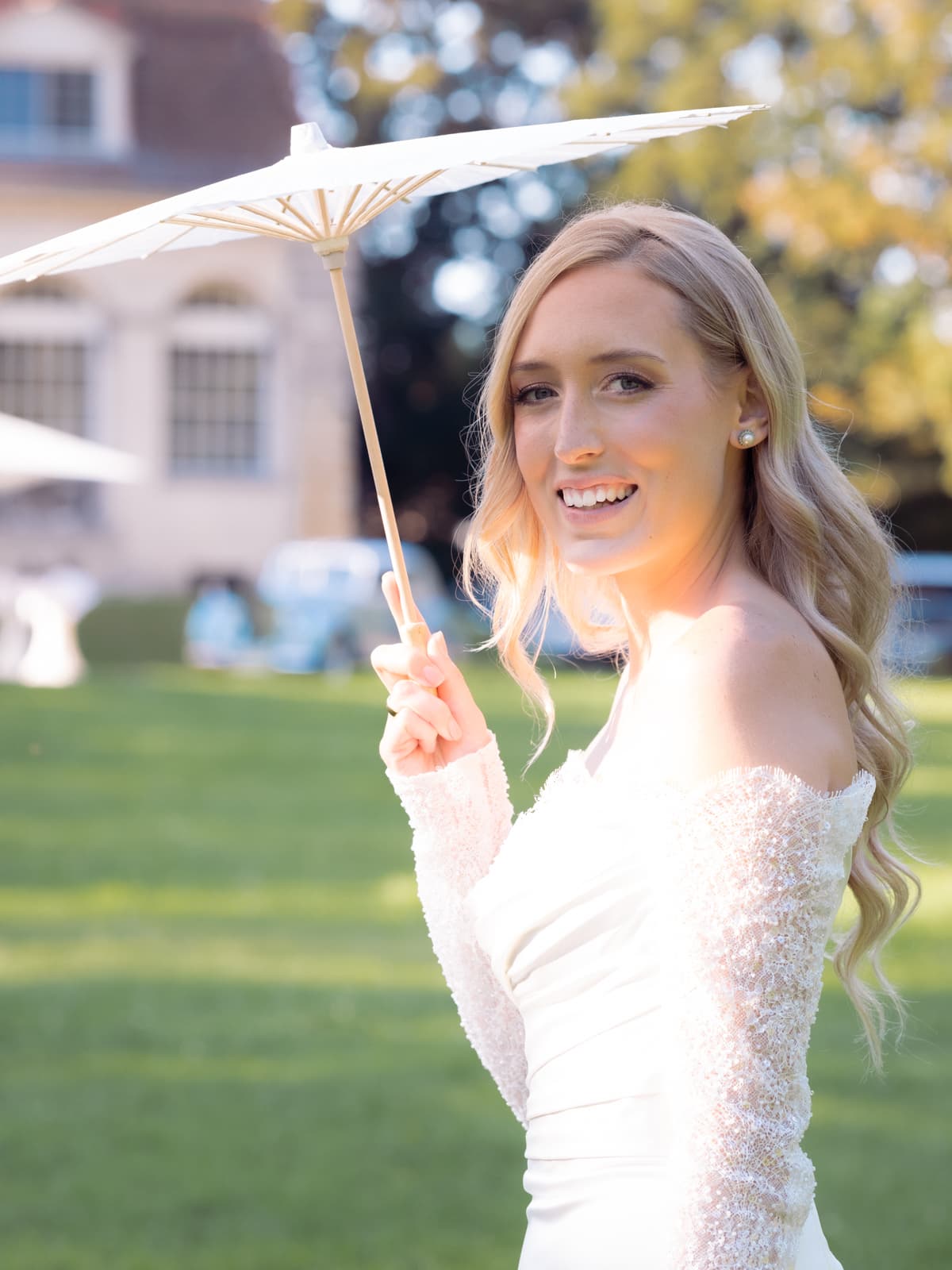 Strahlende Braut hält Sonnenschirm bei sonniger Schloss Kartzow Hochzeit