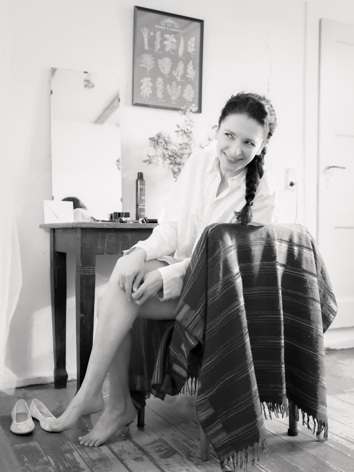 Lächelnde Braut in weißem Seidenhemd bei Hochzeitsvorbereitungen