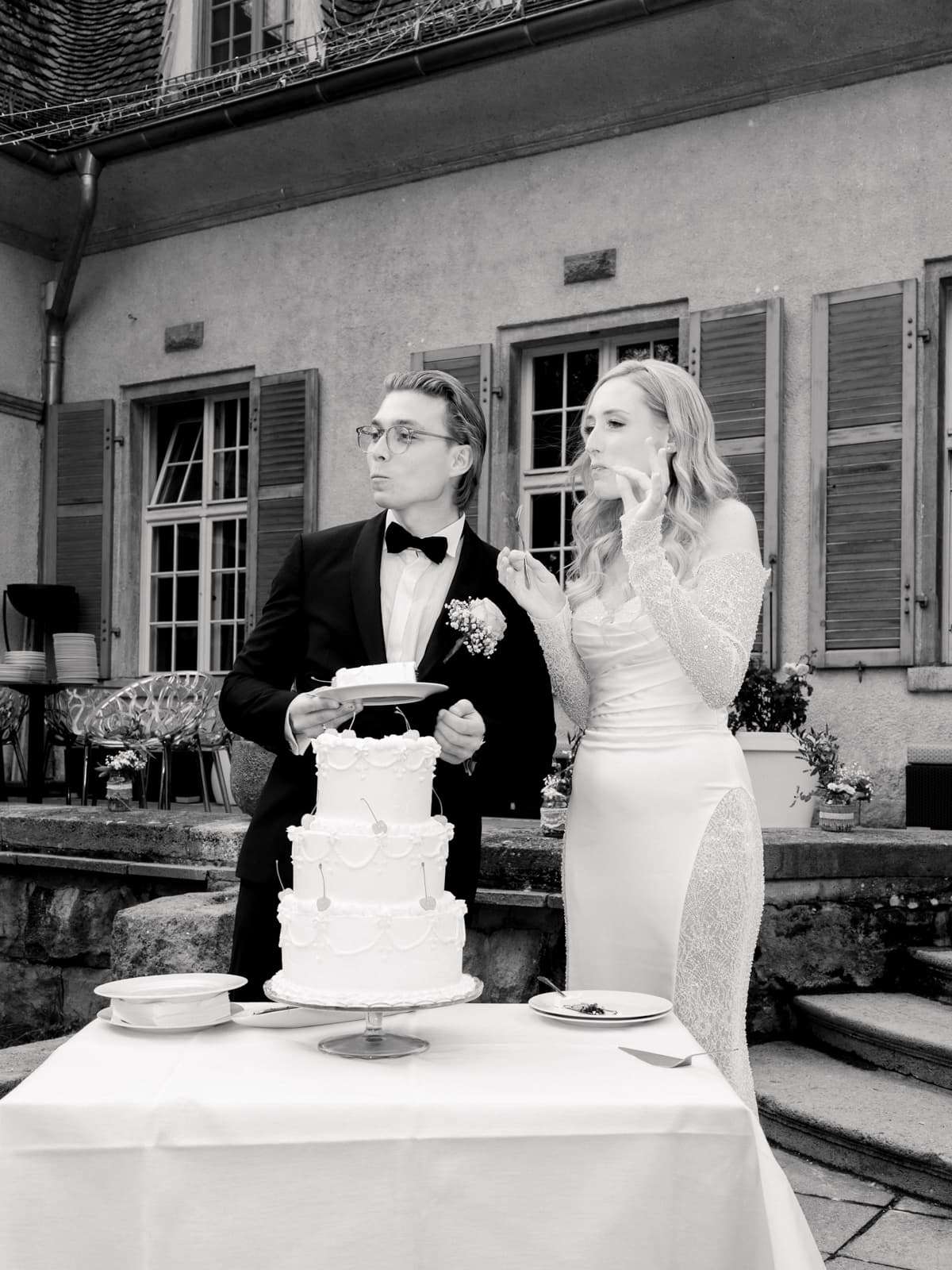 Braut probiert Hochzeitstorte während Bräutigam zuschaut, schwarz-weiß Aufnahme im Schlosshof Kartzow