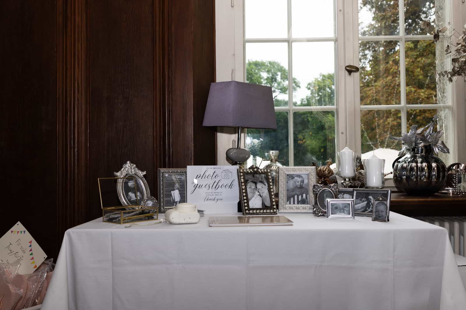 Foto-Gästebuch-Tisch mit gerahmten Fotos und Lampe am Fenster in holzvertäfeltem Raum