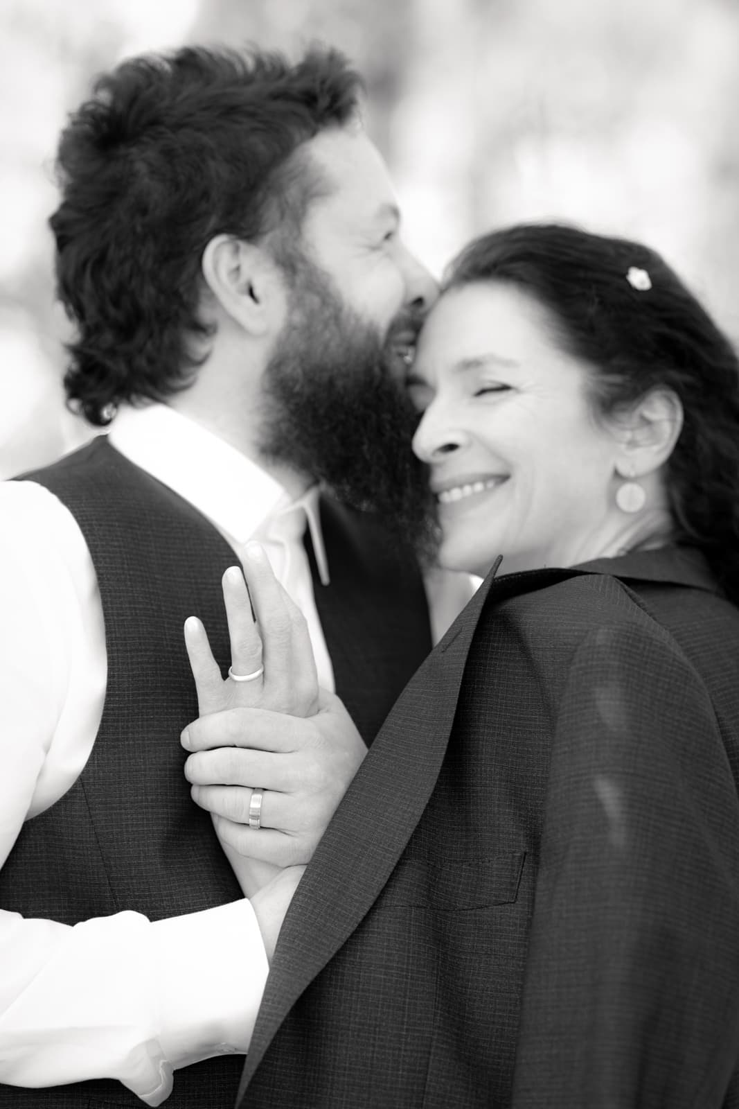 Brautpaar umarmt sich innig bei Hochzeit, Braut lächelt glücklich in schwarz-weiß Hochzeitsfotografie