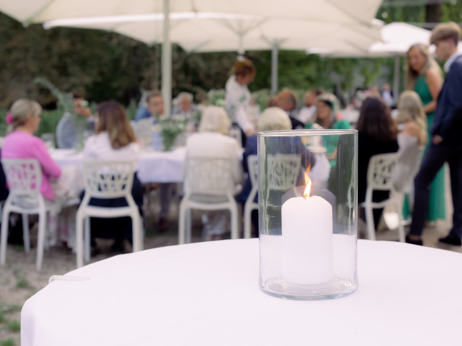 Kerze im Glas vor unscharfen Hochzeitsgästen im Garten - Outdoor Hochzeit Schloss Kartzow