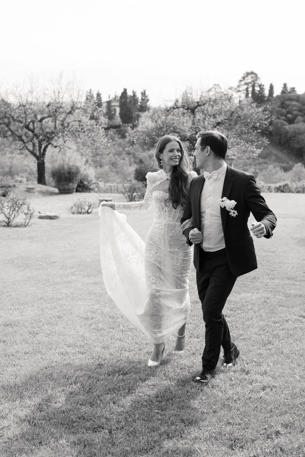 Bride and groom walking hand in hand through a Tuscan garden, black and white